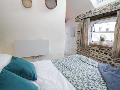 A bedroom with a bed teal pillows white blankets patterned throw and a window with curtains and a potted plant at Dyffryn Cottage in Aberporth