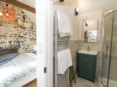 A small bathroom with a sink cabinet mirror and towel rack next to a bedroom with exposed stone walls and a bed at Dyffryn Cottage Aberporth