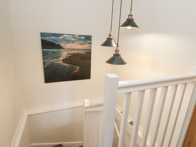 A staircase with white railings three hanging black pendant lights and a beach landscape picture on the wall at Dyffryn Cottage in Aberporth