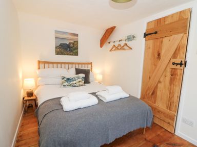 A bedroom with a double bed wooden door bedside lamps and a wall-mounted coat rack at Dyffryn Cottage in Aberporth