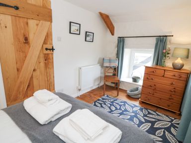 A bedroom with a wooden door a dresser a chair with a blanket and folded towels on the bed at Dyffryn Cottage in Aberporth