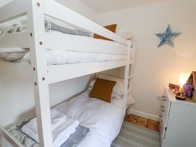 A bedroom with white bunk beds brown pillows a small lamp and toys on a white dresser at Dyffryn Cottage in Aberporth