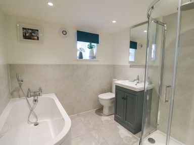 A bathroom with a bathtub shower enclosure toilet sink and small window at Dyffryn Cottage in Aberporth