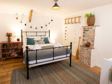 A bedroom with a black metal bed frame a wooden cabinet with flowers a brick fireplace and a wooden ladder on the wall at Dyffryn Cottage Aberporth