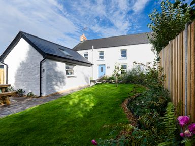 A backyard garden with green grass wooden fence and white buildings at Dyffryn Cottage in Aberporth
