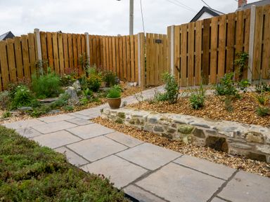 A garden with a stone pathway a stone wall wooden fence and plants at Dyffryn Cottage in Aberporth