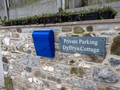 A stone wall with a blue post box and a sign that reads Private Parking Dyffryn Cottage in Aberporth