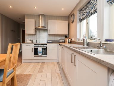 A kitchen with white cabinets a stainless steel oven and hood a sink by a window and a wooden chair at Beech Lodge in Goosnargh