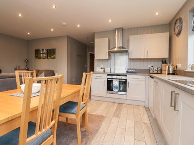A kitchen with wooden dining table and chairs and white cabinets at Beech Lodge in Goosnargh