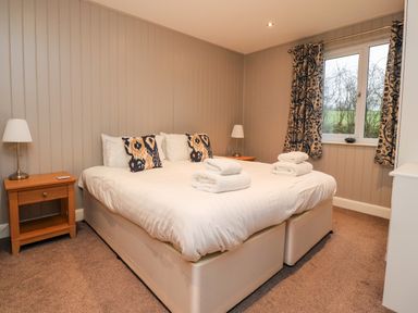A bedroom with a double bed two bedside tables with lamps and a window with patterned curtains at Beech Lodge in Goosnargh