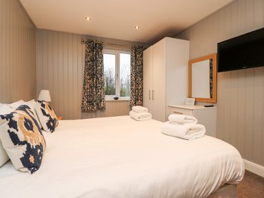 A bedroom with a bed with pillows and towels a white wardrobe a dresser with a mirror and a wall-mounted television at Beech Lodge in Goosnargh
