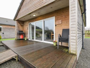Wooden deck with a stacked chairs and a gas grill outside a wooden cabin at Beech Lodge in Goosnargh
