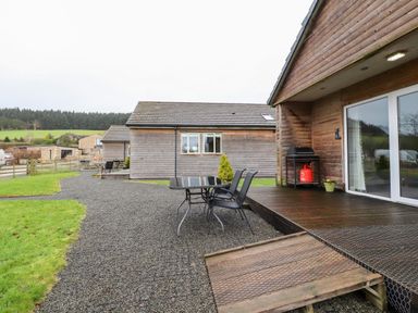 An outdoor area with wooden cabin buildings a gravel pathway a black table with chairs and a wooden deck at Beech Lodge in Goosnargh