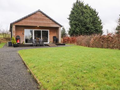 A wooden cabin with a glass sliding door and outdoor seating on a lawn at Beech Lodge in Goosnargh