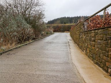 A concrete driveway with a stone wall on the right and bushes on the left at Beech Lodge in Goosnargh