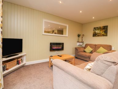 A living room with two sofas a wooden coffee table a wall-mounted electric fireplace and a television at Oak Lodge in Goosnargh