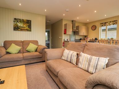 A living room with two brown sofas and cushions near a kitchen with wooden chairs and cabinets at Oak Lodge in Goosnargh