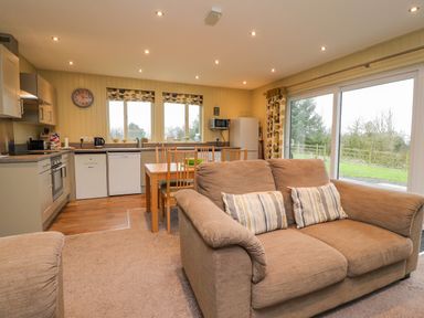 An open kitchen and dining area with a beige sofa and sliding glass doors at Oak Lodge in Goosnargh