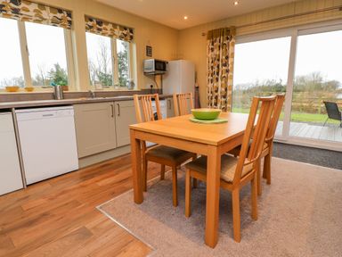 A kitchen with wooden dining table and chairs next to sliding glass doors at Oak Lodge in Goosnargh