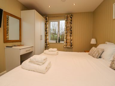 A bedroom with a bed towels a wardrobe a desk a mirror and a window with curtains at Oak Lodge Goosnargh