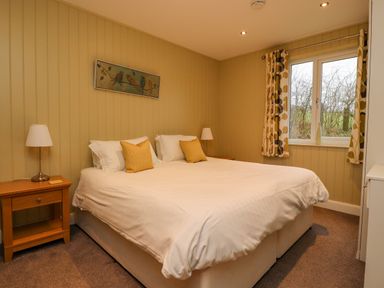 A bedroom with a double bed yellow pillows bedside tables lamps and a window with patterned curtains at Oak Lodge in Goosnargh