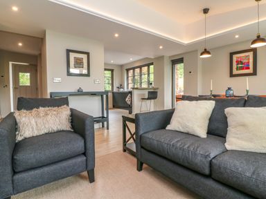 A living room with dark gray sofa and armchair with cushions and a dining area with table and chairs at Court Lodge in Bathealton near Wiveliscombe