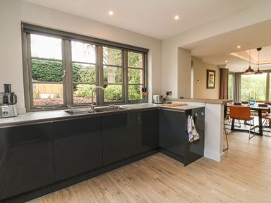 A kitchen with black cabinets and a sink under large windows next to a dining area with chairs at Court Lodge in Bathealton near Wiveliscombe