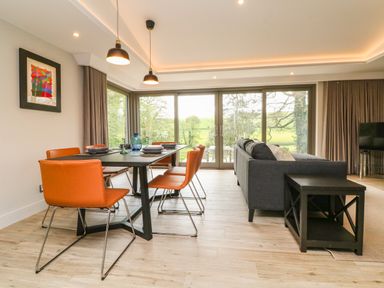 A dining area with orange chairs and a black table next to a living room with a gray sofa and a black side table at Court Lodge in Bathealton near Wiveliscombe