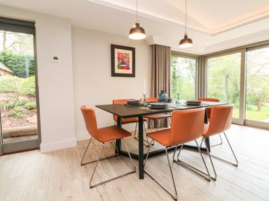 A dining room with six orange chairs and a black table near large windows at Court Lodge in Bathealton near Wiveliscombe