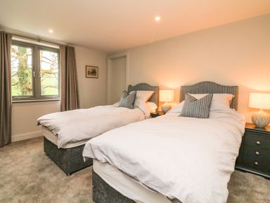 A bedroom with two single beds bedside tables lamps and a window at Court Lodge in Bathealton near Wiveliscombe