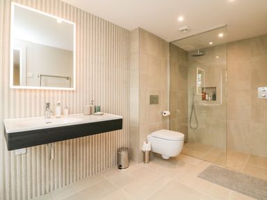 A bathroom with a wall-mounted sink and mirror a wall-mounted toilet and a walk-in shower at Court Lodge in Bathealton near Wiveliscombe