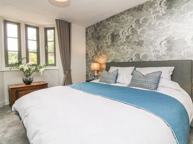 A bedroom with a bed pillows a lamp beside the bed and windows with curtains at Court Lodge in Bathealton near Wiveliscombe