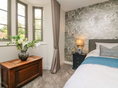 A bedroom with a bed a bedside table with a lamp and a wooden chest under windows at Court Lodge in Bathealton near Wiveliscombe