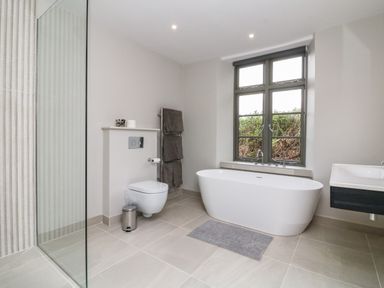 A bathroom with a freestanding bathtub a wall-mounted toilet and a glass shower enclosure at Court Lodge in Bathealton near Wiveliscombe