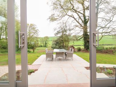 A patio with a table and four chairs looking out to a garden and trees at Court Lodge in Bathealton near Wiveliscombe