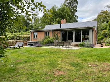 A garden with green lawn lounge chairs and outdoor dining table by a house at Court Lodge in Bathealton near Wiveliscombe