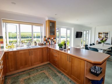 A kitchen with wooden cabinets and a countertop overlooking a window with a view of green fields at Newquay Tamarisk Lodge on the Gannel in Newquay