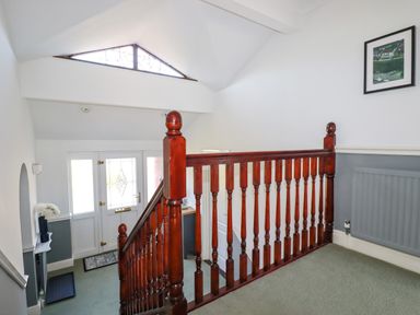 A stairway with wooden railing leading down to an entrance door with decorative glass panels at Newquay Tamarisk Lodge on the Gannel in Newquay
