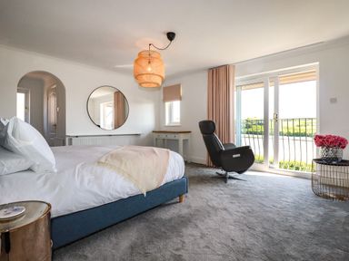 A bedroom with a bed chair round mirror and a side table with flowers at Newquay Tamarisk Lodge on the Gannel in Newquay