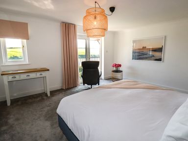 A bedroom with a bed a desk a black chair pink curtains and a round side table with flowers at Newquay Tamarisk Lodge on the Gannel in Newquay