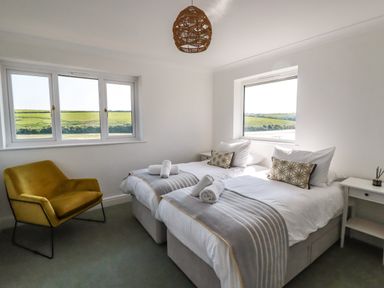 A bedroom with two single beds a yellow armchair and windows showing a green field at Newquay Tamarisk Lodge on the Gannel in Newquay