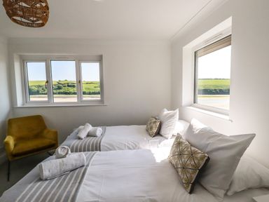 A bedroom with two single beds pillows and towels next to two windows and a yellow armchair at Newquay Tamarisk Lodge on the Gannel in Newquay