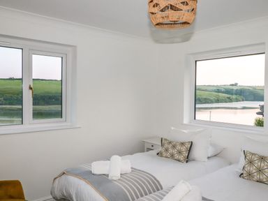 A bedroom with two single beds and windows showing a river and green hills at Newquay Tamarisk Lodge on the Gannel in Newquay