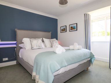 A bedroom with a double bed pillows rolled towels two pictures on the wall and a window with striped curtains at Newquay Tamarisk Lodge on the Gannel in Newquay