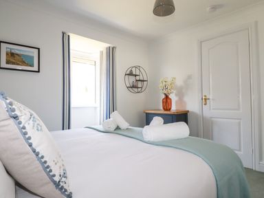 A bedroom with a bed rolled towels on the bed bedside table with flowers wall art and a window at Newquay Tamarisk Lodge on the Gannel in Newquay