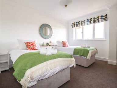 A bedroom with two single beds green throws and floral pillows at Newquay Tamarisk Lodge on the Gannel in Newquay