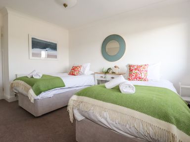 A bedroom with two single beds with green throws and floral pillows at Newquay Tamarisk Lodge on the Gannel in Newquay