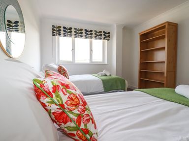 A bedroom with two single beds with floral pillows and green blankets and a wooden bookshelf at Newquay Tamarisk Lodge on the Gannel in Newquay