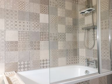 A bathtub with a showerhead and patterned tiles on the wall at Newquay Tamarisk Lodge on the Gannel in Newquay