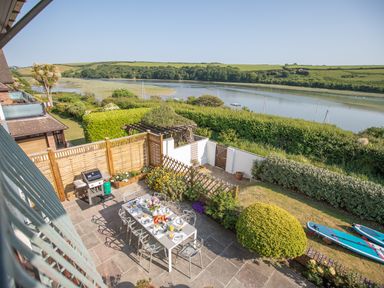 An outdoor patio area with a dining table set for breakfast a barbecue grill garden plants and a river view at Newquay Tamarisk Lodge on the Gannel in Newquay